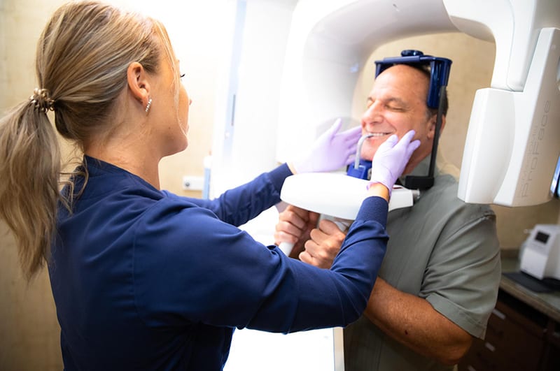 Experienced Cape Dental Care staff member giving smiling patient a CT scan to use for a dental implant consultation for a personalized dental plan