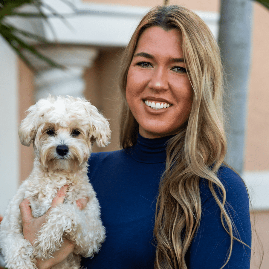 Dr. Linda Kornienko smiling as she poses for a headshot in front of a palm tree at the Cape Dental Care office while holding her dog