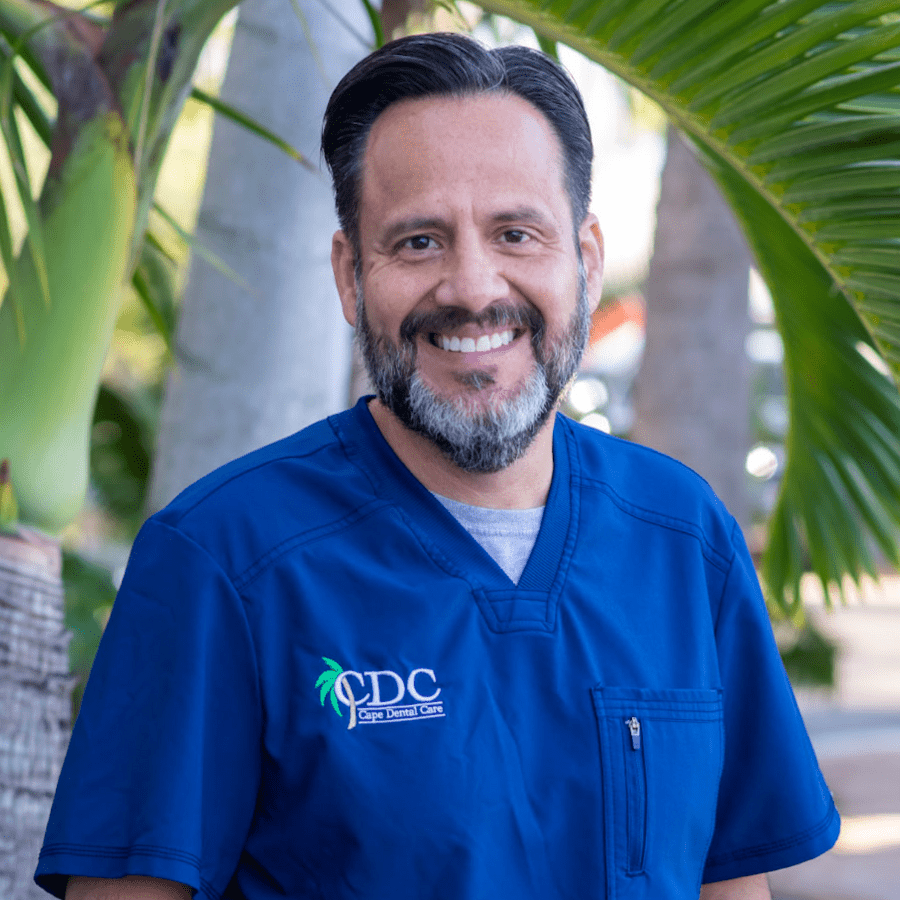 Dr. Mario Romero smiling as he poses for a headshot in front of some palm trees