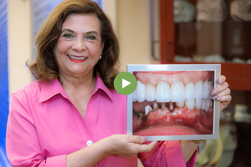 Woman smiling after a successful dental implant and bone graft procedure while holding a before picture
