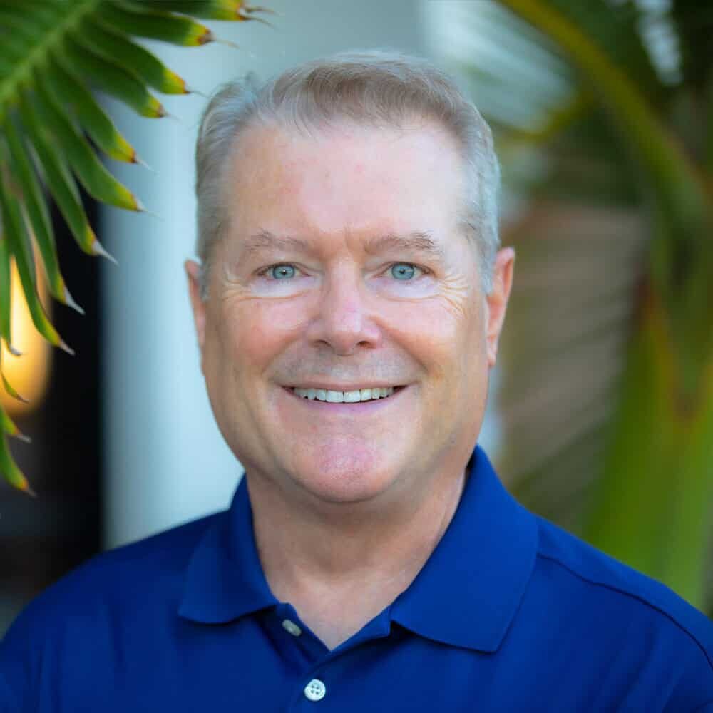 Dr. Mark Kraver smiling as he poses for a headshot in front of some palm trees
