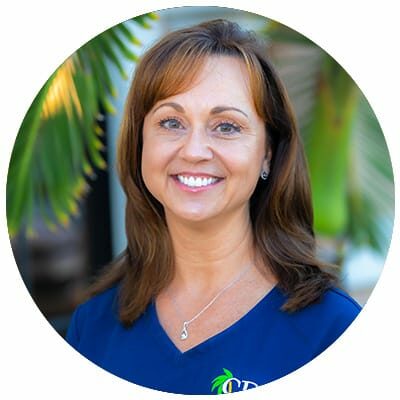 Hygienist Julie smiling as she poses for a headshot in front of palm trees