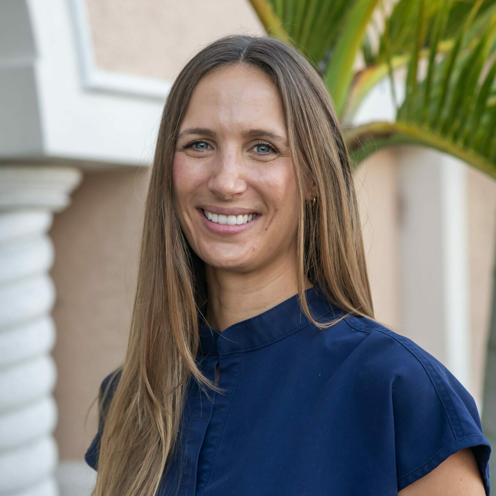 Dr. Lindsey Balaban smiling as she poses for a headshot in front of a palm tree at the Cape Dental Care office